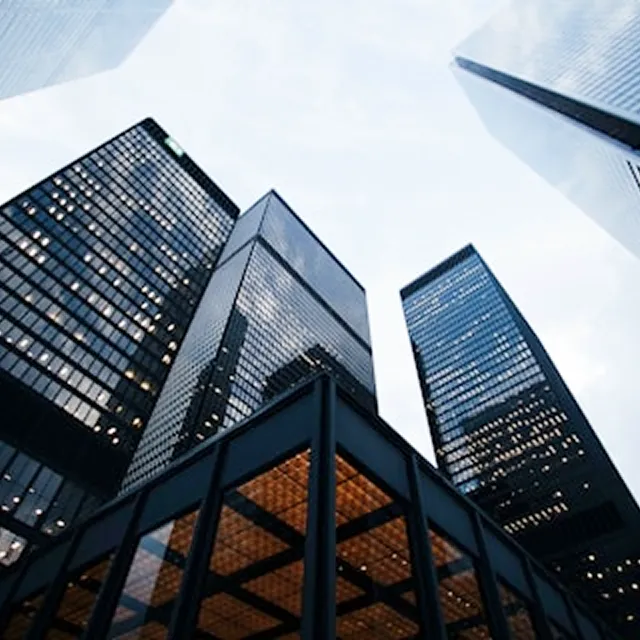 真下から見上げた複数の高層ビル群。ガラス張りの外壁が青空を反射し、都会的な洗練さと建物の高さを強調している構図